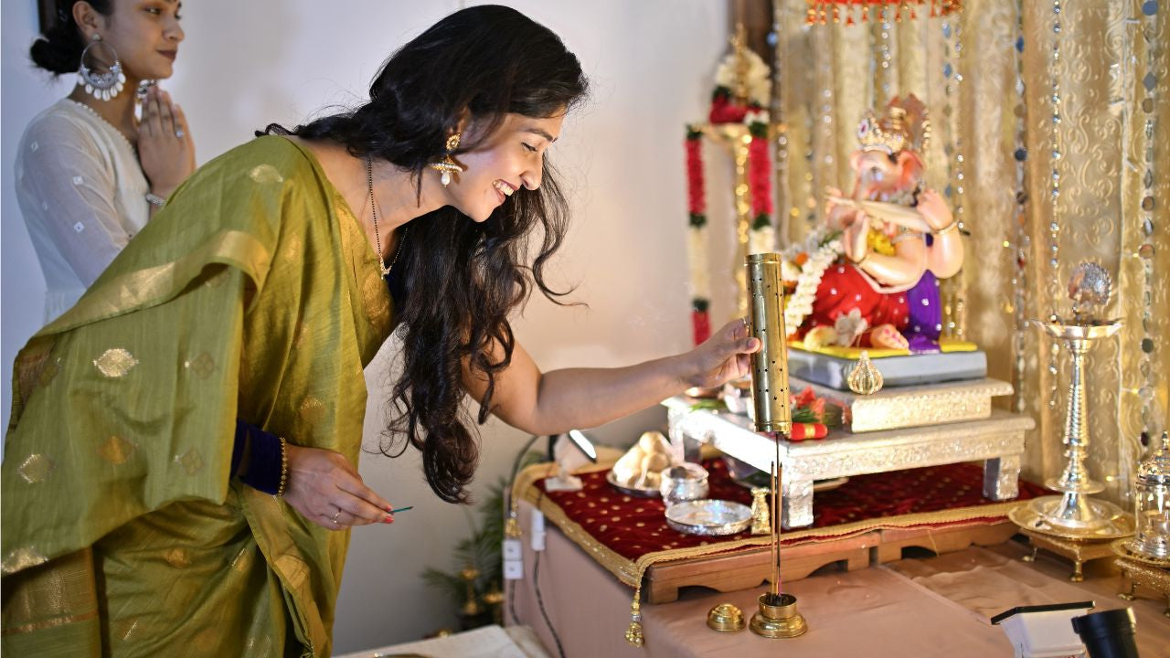 Woman in a green saree performing a ritual with a deity statue in a decorated room.